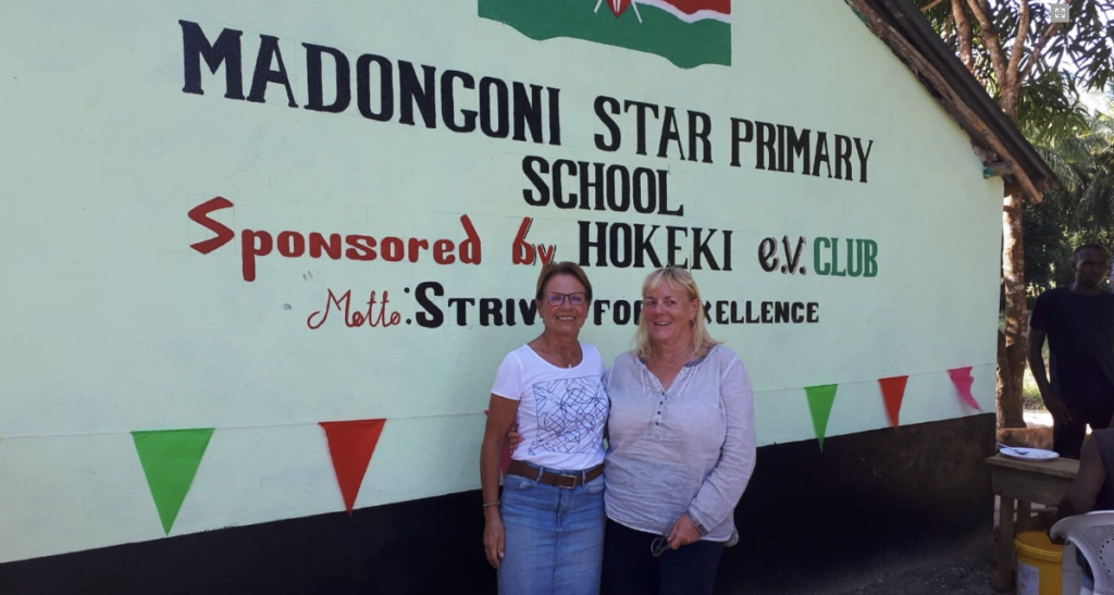 Zwei Vereinsmitglieder vor dem beschrifteten Giebel der Madongoni Star Primary School zur Einweihung des ersten Bauabschnitts