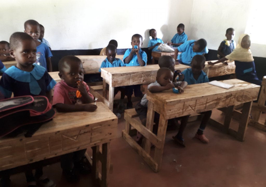 Schulkinder sitzen an den neu gebauten Holzbänken im Klassenraum der Madongoni School