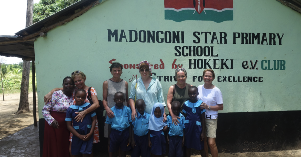 Mitglieder des HOKEKI e.V. stehen mit Schulkindern vor dem Giebel der Madongoni Star Primary School