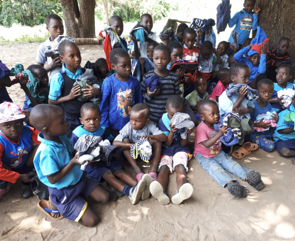 Kinder in Kenia sitzen im Sand und packen die aus Erfurt gespendeten Schuhe und Kleidungsstücke aus